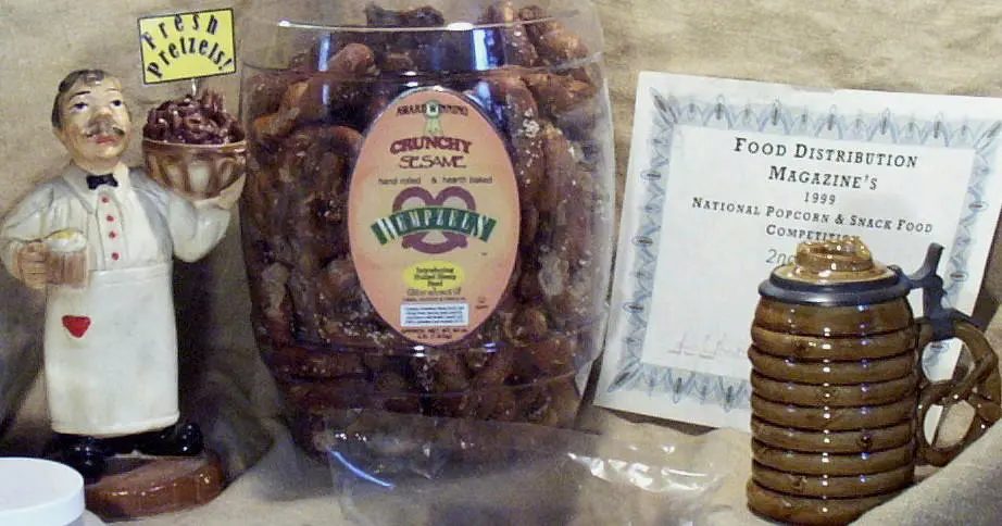 Barrel of Hempzels Sesame Sourdough next to a statue of a baker next to an award from 1999 by Food Distribution for best pretzel