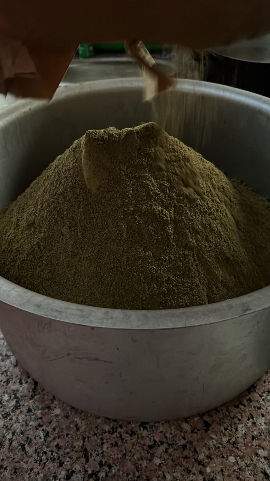 Hemp flour piled very high, brown green color with front of large bowl edge.